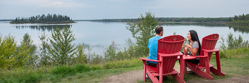 Deux visiteurs profitent de la vue sur le lac Astotin depuis des chaises rouges emblématiques de Parcs Canada.