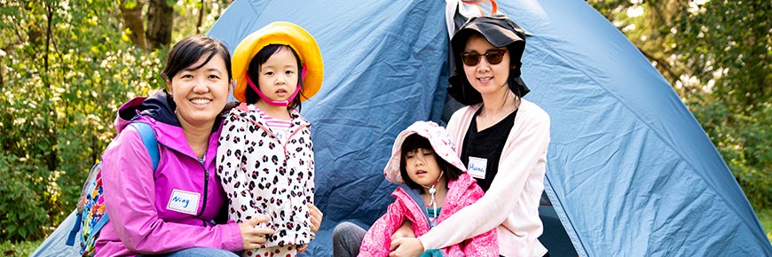 Two mothers with their daughters pose in front of a tent