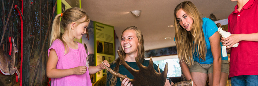 A Parks Canada staff member holding a moose antler smiles at interested children in the Astotin Theatre.