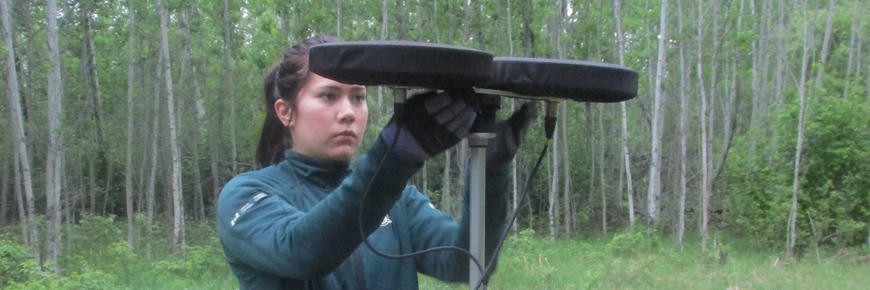 A Parks Canada staff member sets up a stereo microphone in the forest. 