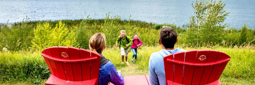Une famille profite de deux chaises rouges emblématiques de Parcs Canada pour admirer la vue du lac Astotin. 