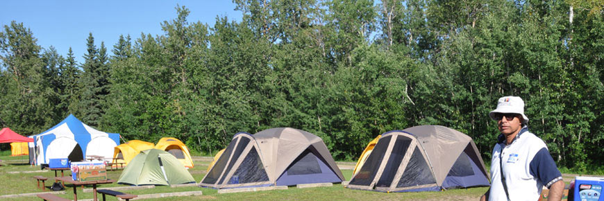 Plusieurs tentes de toutes les couleurs éparpillées sur un terrain bordé d’arbres.
