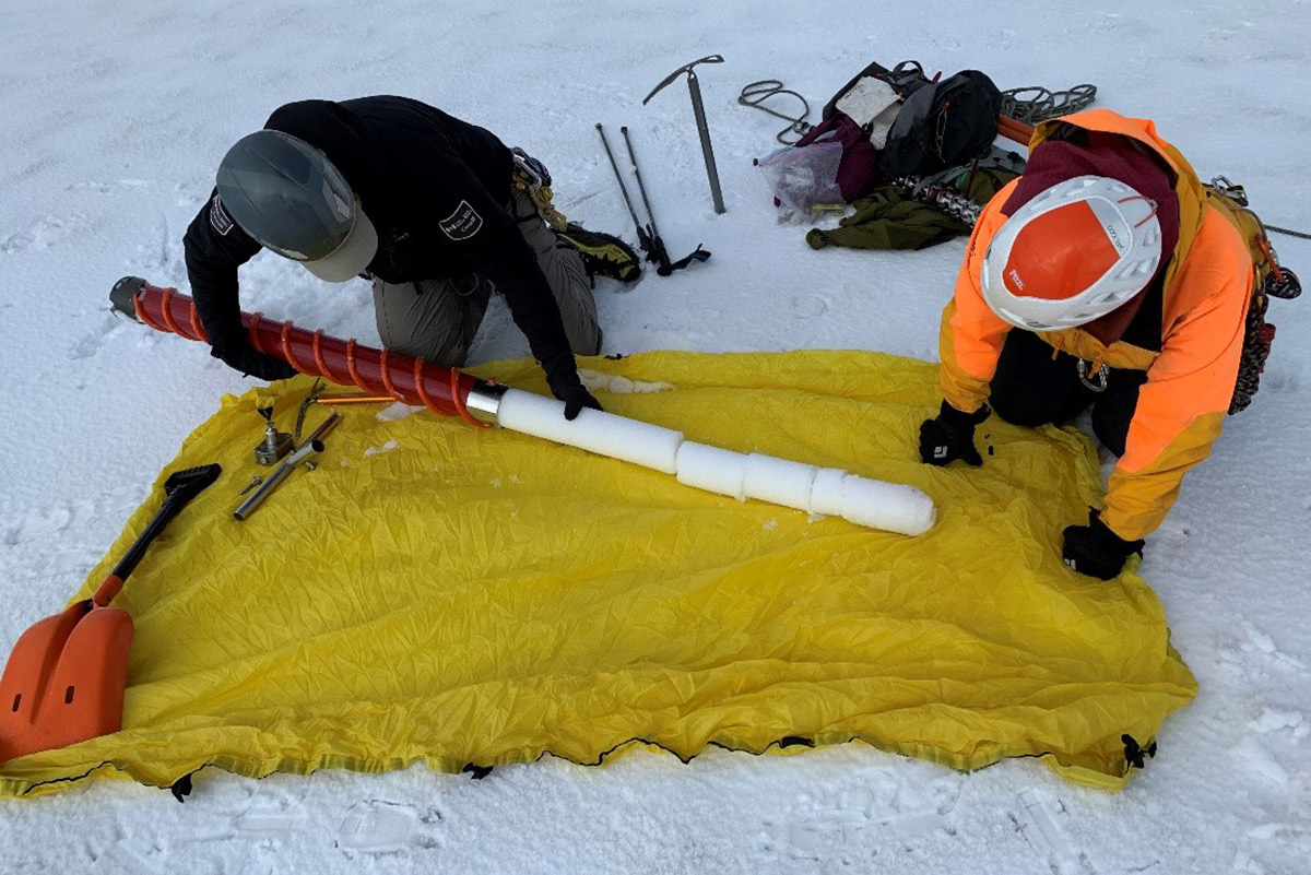Two people with glaciology tools taking snow measurements in the field