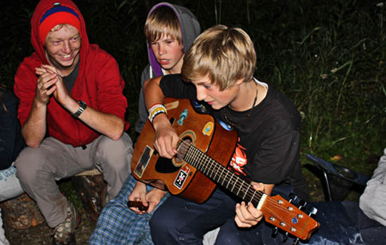 Un étudiant joue de la guitare auprès du feu pendant que deux autres regardent