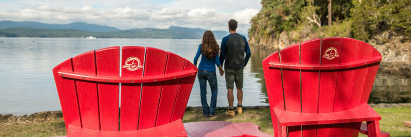 Two red chairs at Gulf Islands National Park Reserve with a couple looking at the ocean.