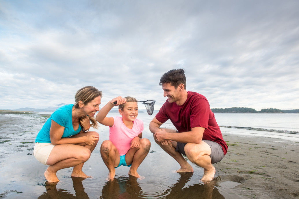 Three people on a beach. Two adults look at their child. The child is holding a net.