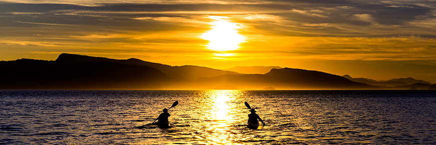 Two kayakers paddle into the sunset off Pender Island