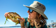 Une membre du personnel de Parcs Canada sourit à pleines dents et tient avec soin un gros crabe dans sa main.