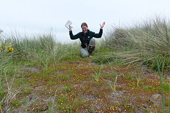 Une biologiste du parc lève les bras dans un geste de célébration près d’un tapis de petites fleurs jaunes poussant sur le sable.