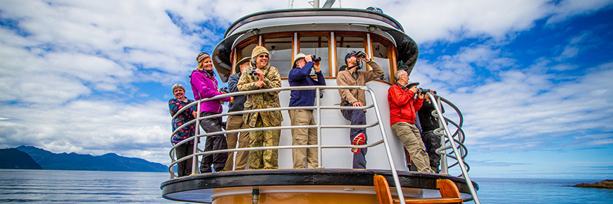 A tour group looks out over the ocean from the bridge of the boat. 3 of them are using binoculars.