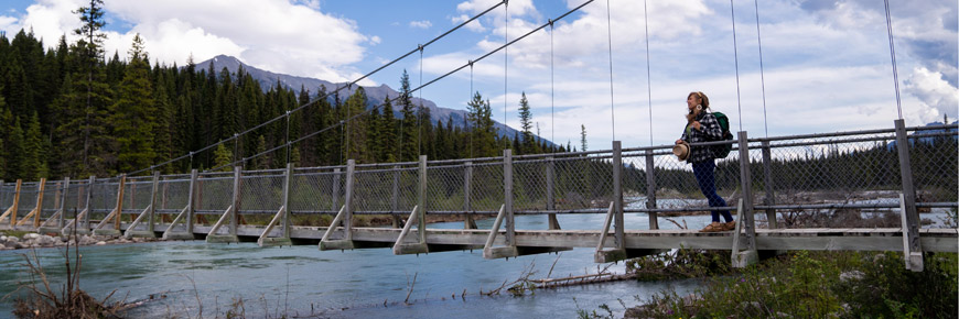A hiker stands on a suspension bridge over Kootenay River enjoying the view