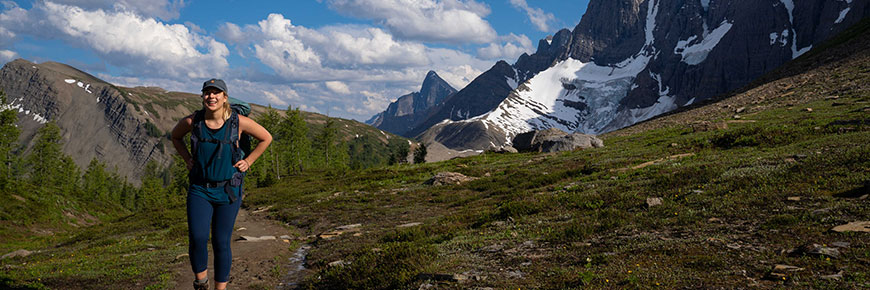 A hiker travels on the Tumbling Pass trail with towering peaks and glaciers in the background