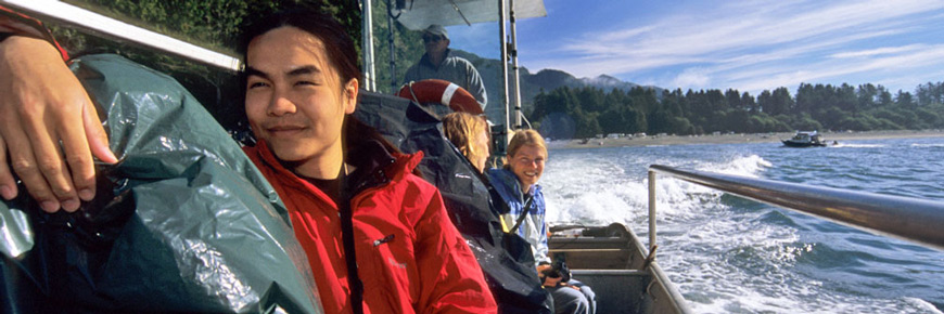 Hiker sits at front of water taxi with two hikers and captain behind them. Shoreline and forest on horizon in background.