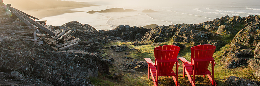 Two red chairs in Pacific Rim National Park Reserve overlooking the Pacific Ocean at sunset. 