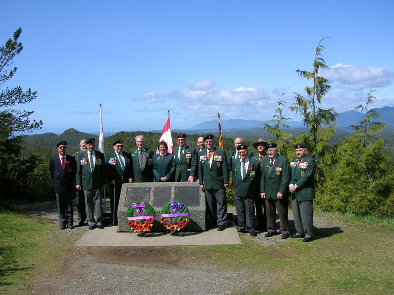 Des officiers se tiennent sur la colline Radar près du monument commémoratif, entourés de drapeaux et de couronnes