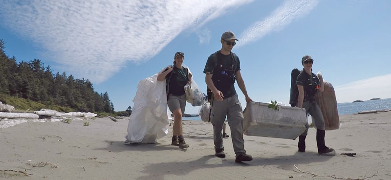 Three Parks Canada employees carrying marine debris along sandy beach.