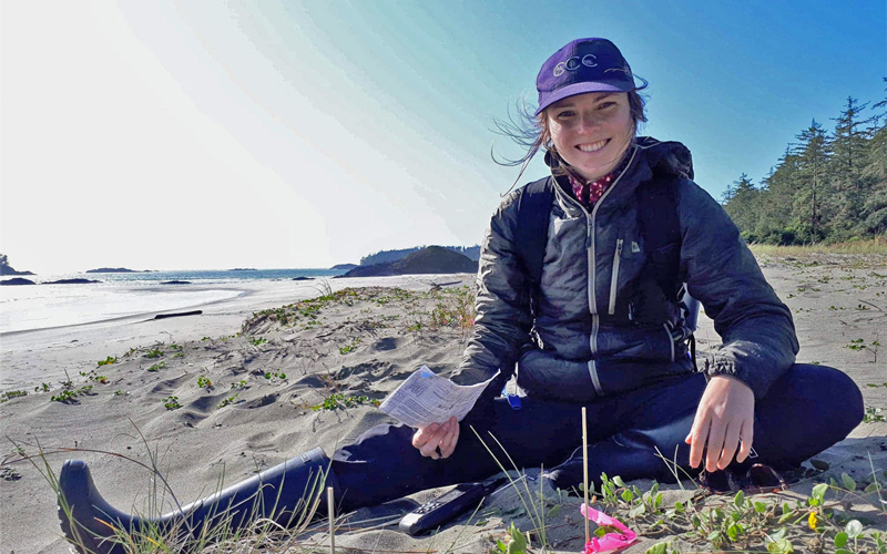 Jeune volontaire assis dans les dunes de sable à compter les plantes.