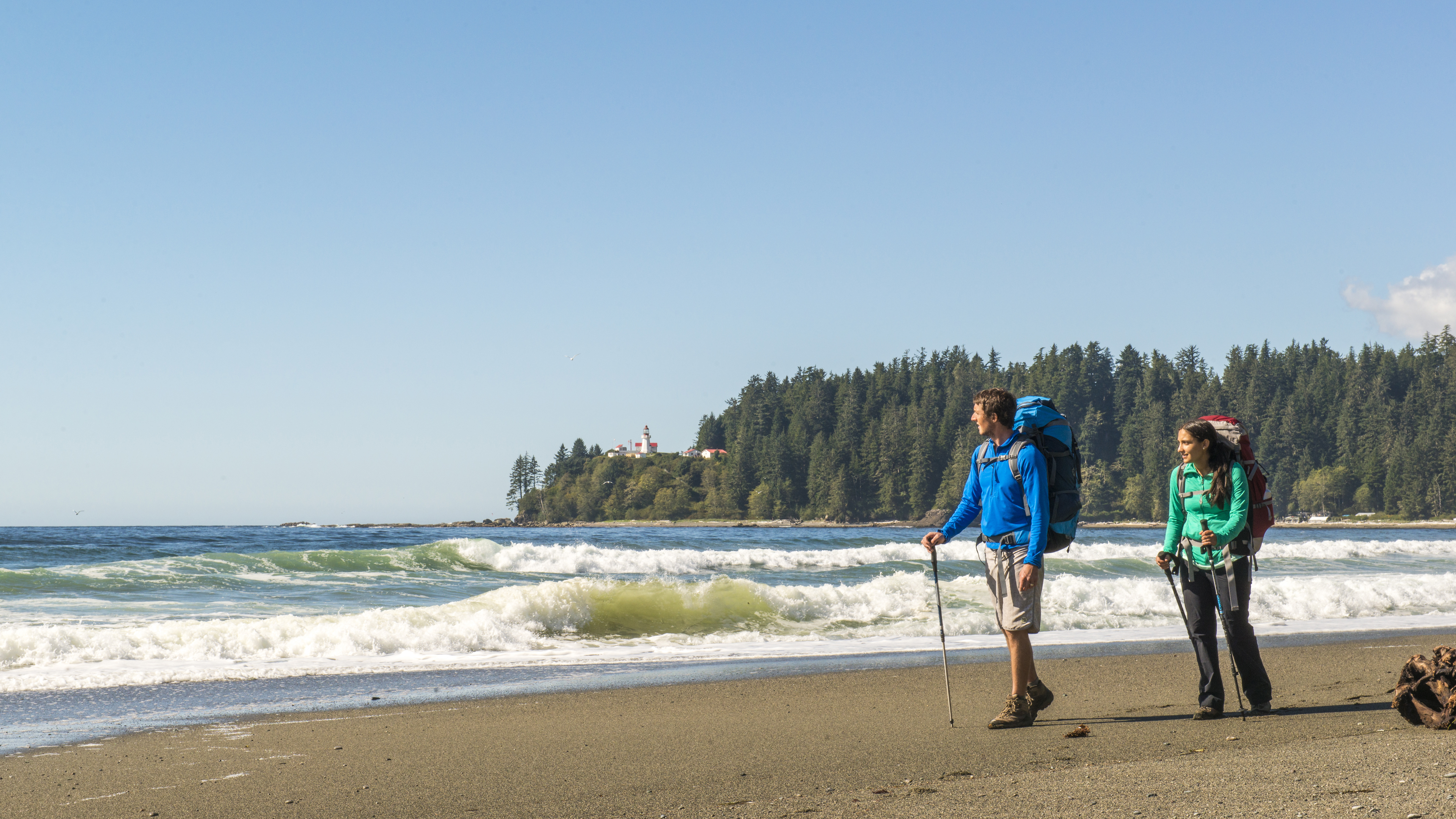 Two hikers with backpacks walking on the beach on the West Coast Traill