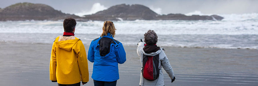 Three people in raingear looking out to a stormy beach