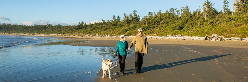 Two people walking their dog on leash on Wickaninnish Beach