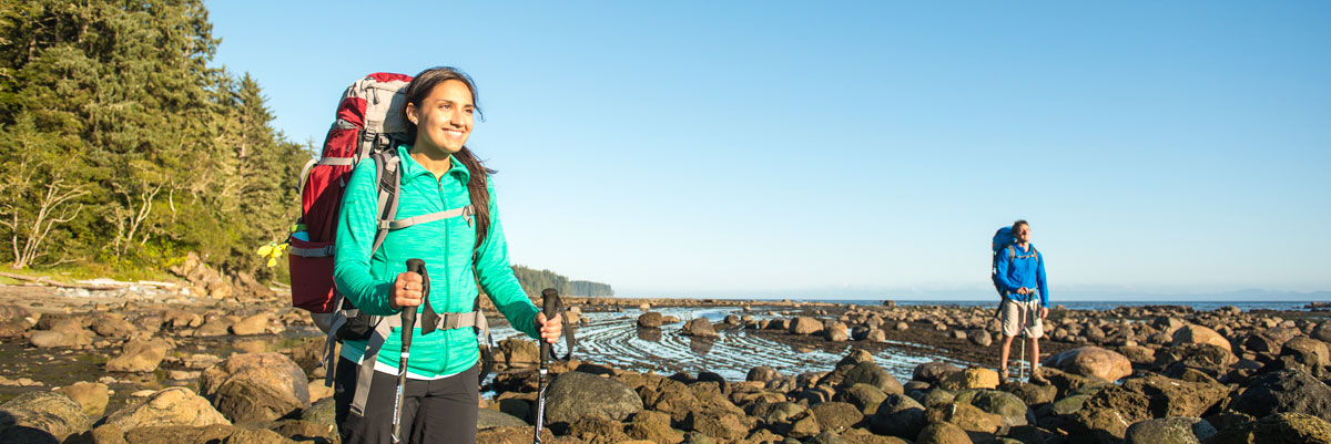 Hiker with pack and hiking poles in foreground and additional hiker in background on a rocky beach