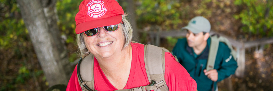 Une bénévole portant un chandail et chapeau rouge de Parcs Canada sur un sentier en forêt