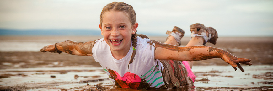 A girl sliding on her stomach in the muddy beach water