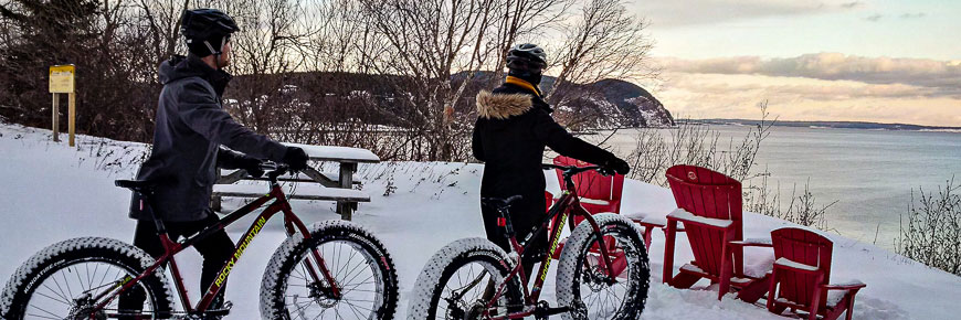 A couple on fatbikes in the snow next to red chairs