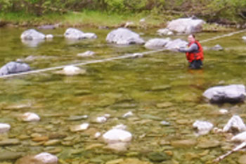 Un randonneur traverse un cours d’eau en tenant une corde.