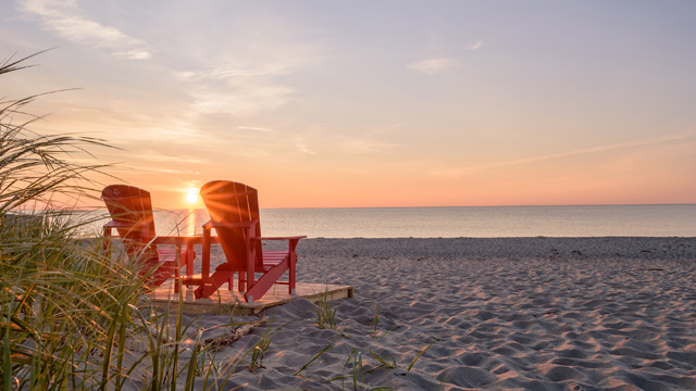 Deux chaises rouges de Parcs Canada sur une plage de sable au lever du soleil.
