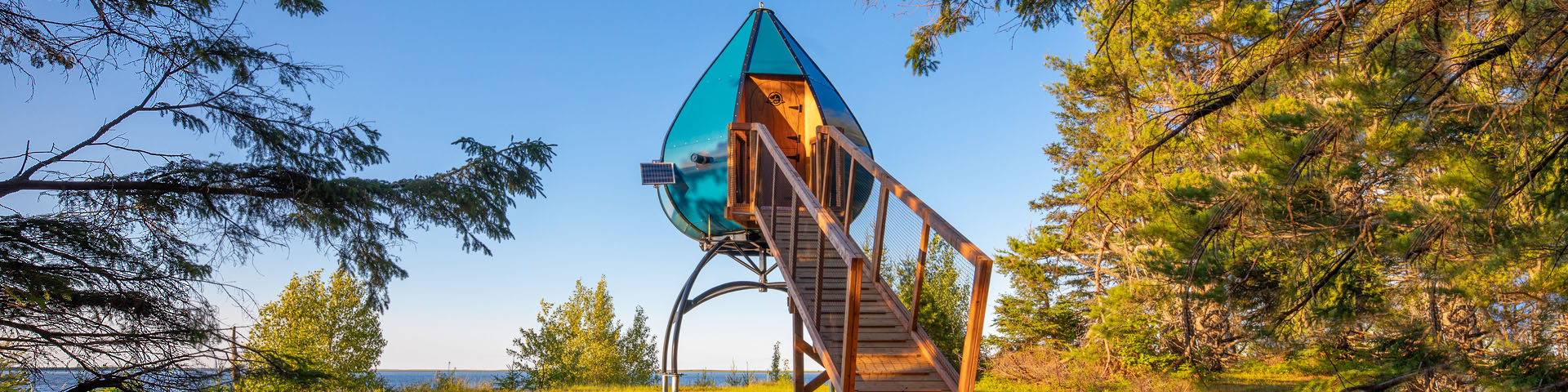 A tear drop-shaped camping accommodation in the woods near a body of water.