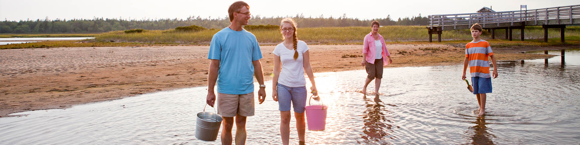 A family walks in the shallow water with scoops and buckets, fishing clams