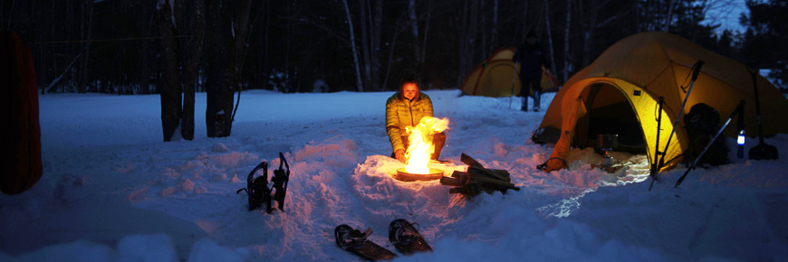 A lady warming up in front of a campfire in the snow