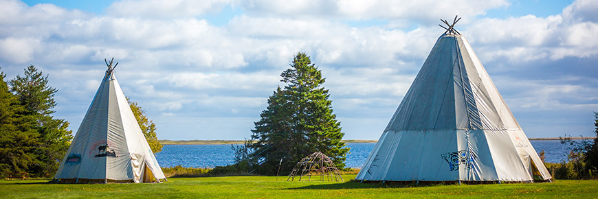 Two wigwam in a field next to a lagoon