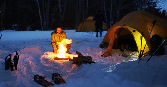 A lady warming up in front of a campfire in the snow