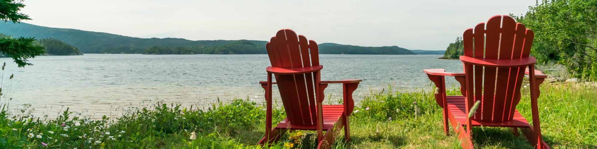 deux chaises Adirondack rouges donnant sur un bras de mer
