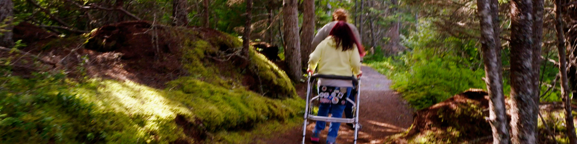 two people (one using a walker) walking along a forested trail