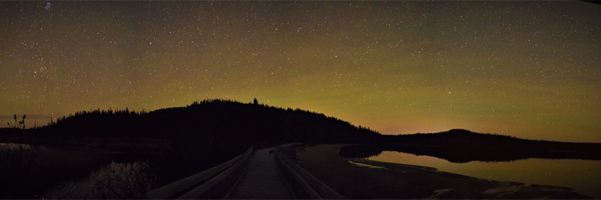 a starry, night sky over a bridge next to a pond