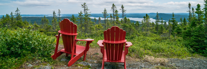 two red Adirondack chairs overlooking a forested coastal scene