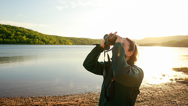 A person standing seaside looking through binoculars