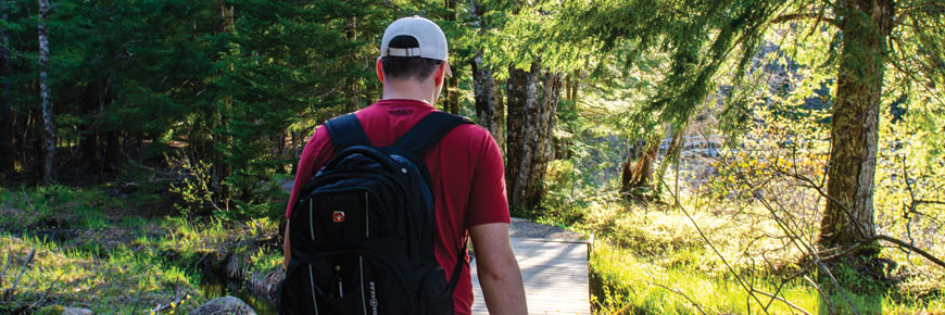 Un homme en randonnée dans les bois portant un chapeau et un sac à dos.