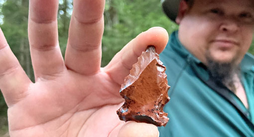 Un guide de Parcs Canada montre une pointe de flèche en silex qu’il tient dans la main.