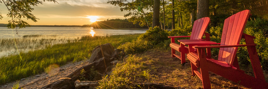 Chaises rouges de Parcs Canada et vue sur le coucher de soleil au bord d’un lac. 