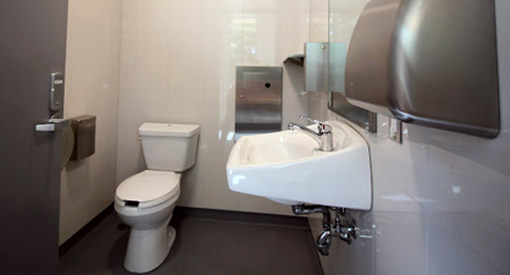 The standard washroom has a toilet, sink, soap dispenser, mirror, waste bin, hand-drying station, and braille signage on the door.