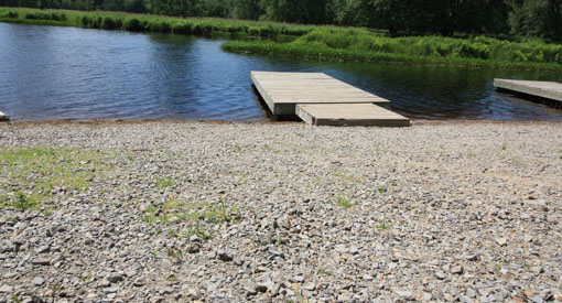 Crushed rock next to a floating river dock with plastic docking platform and a wooden section.