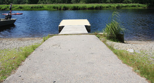 Chemin d’asphalte menant vers un quai flottant sur la rivière composé d’une plateforme de quai de plastique et d’une section en bois.