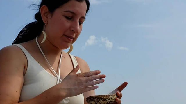A woman holding a shell with sage for a smudging.