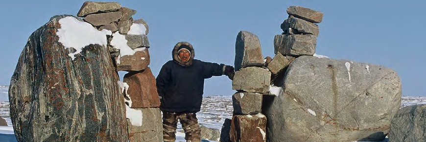 A man standing between two rock cairns, or inuksuit.