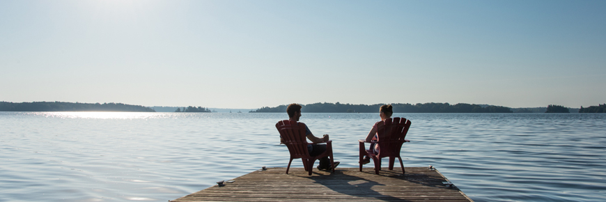 Two people relax on in red chairs on the end of the dock