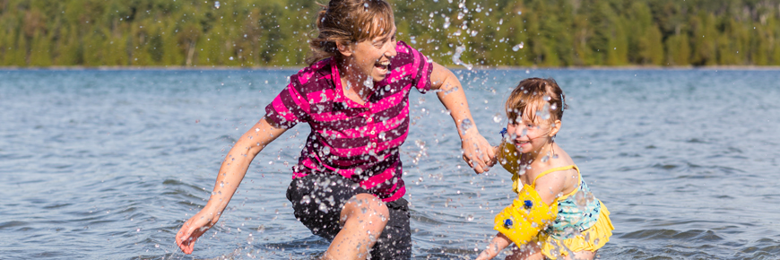 A mother and daughter splash in the shallow water. 